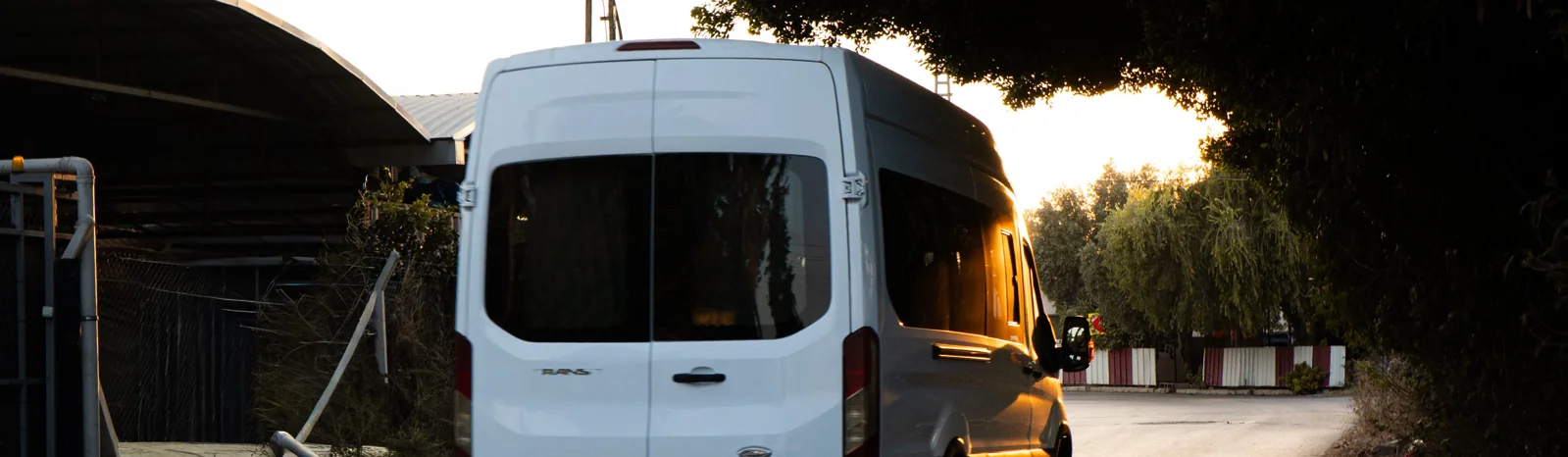 A white long-wheelbase courier van on a quiet country lane at dusk.